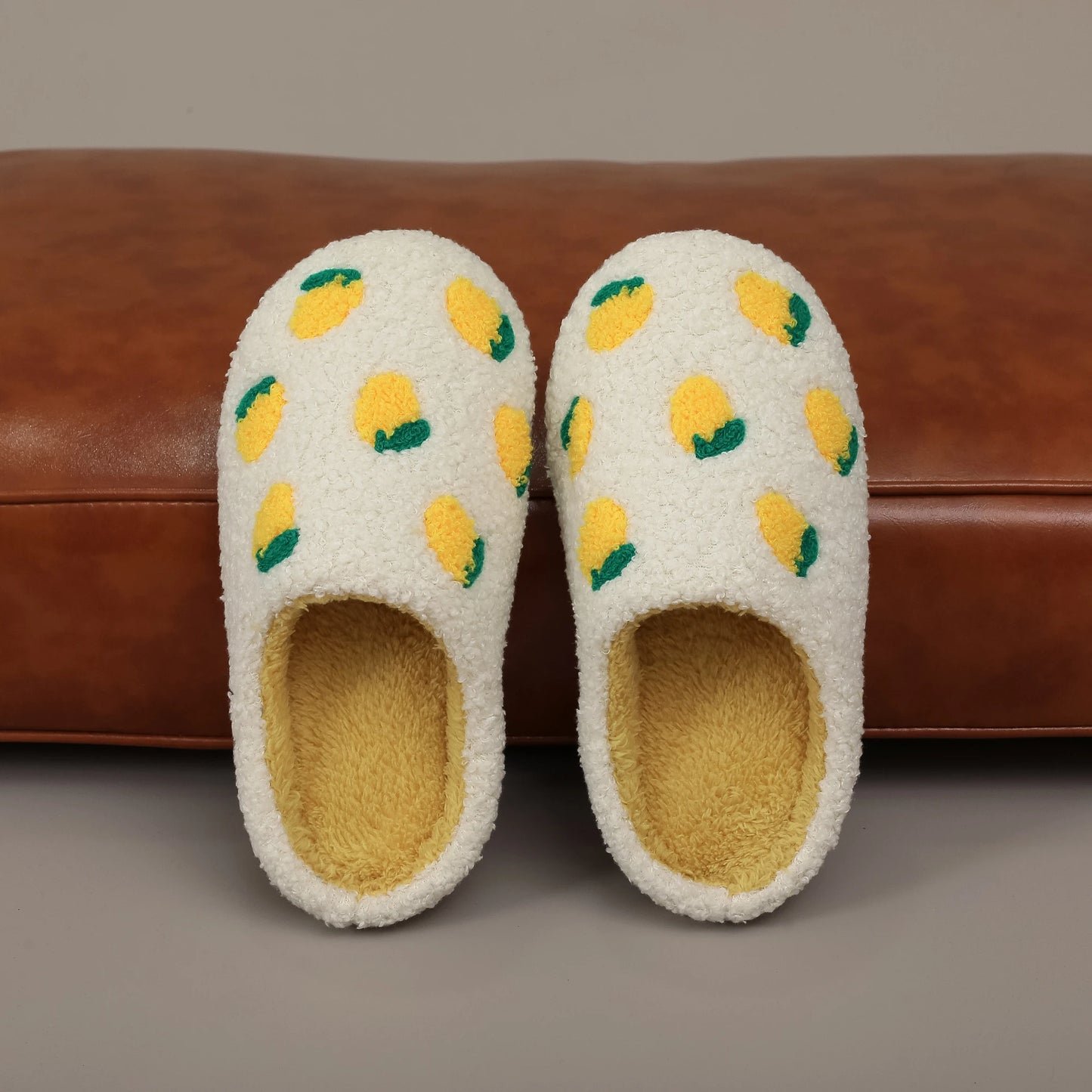 Pair of white slippers with lemon pattern on a brown surface