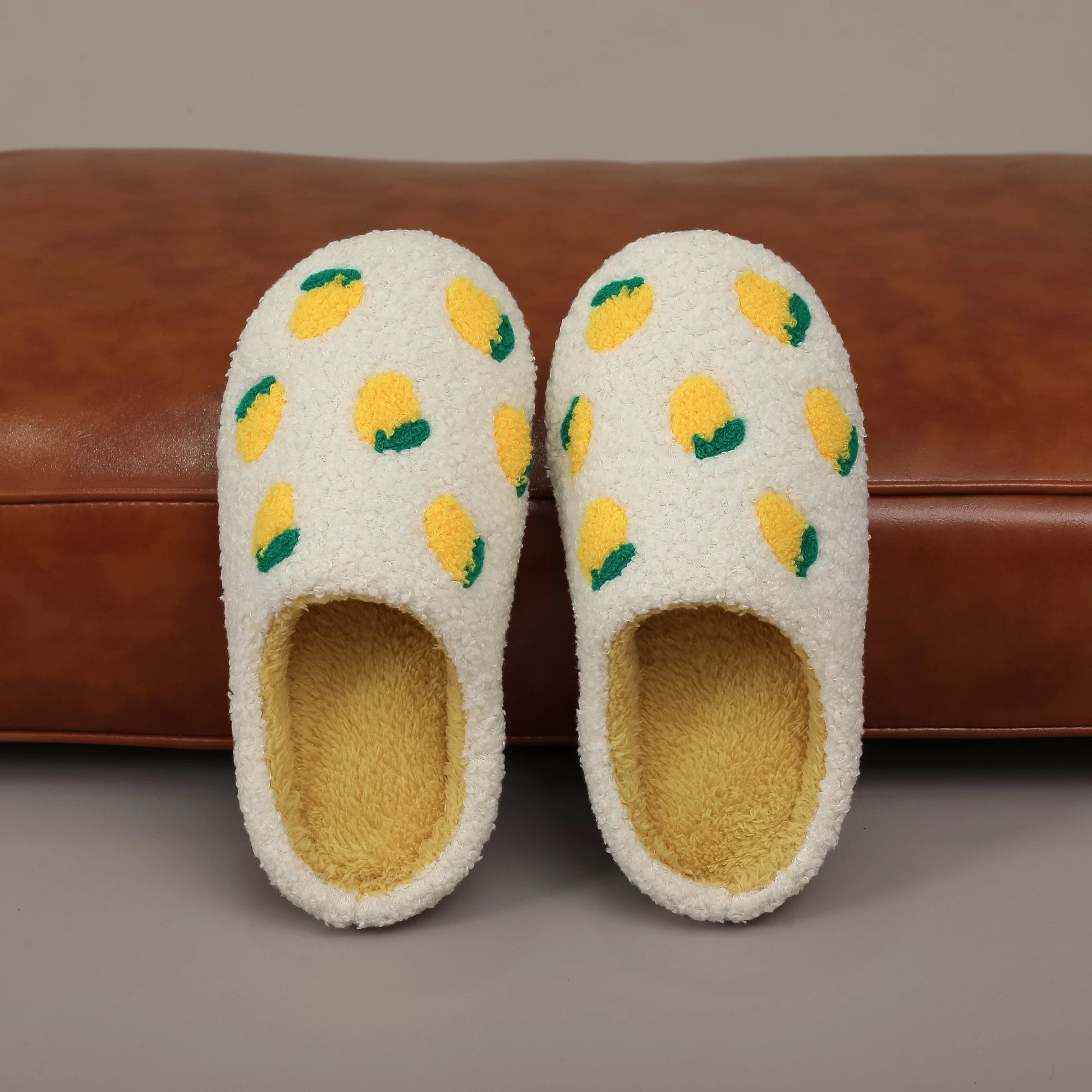 Pair of white slippers with lemon pattern on a brown surface