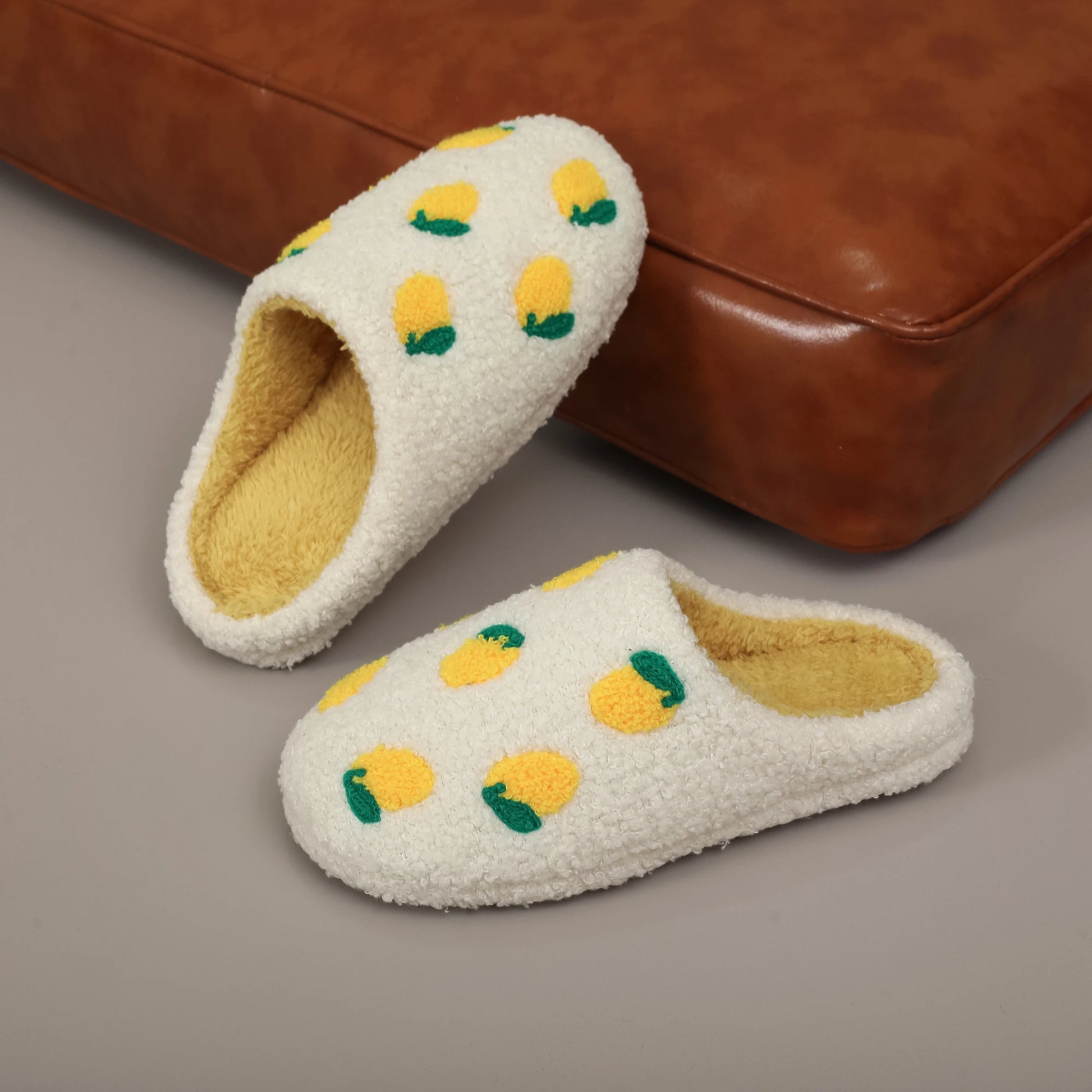 Pair of white slippers with lemon design on a brown surface