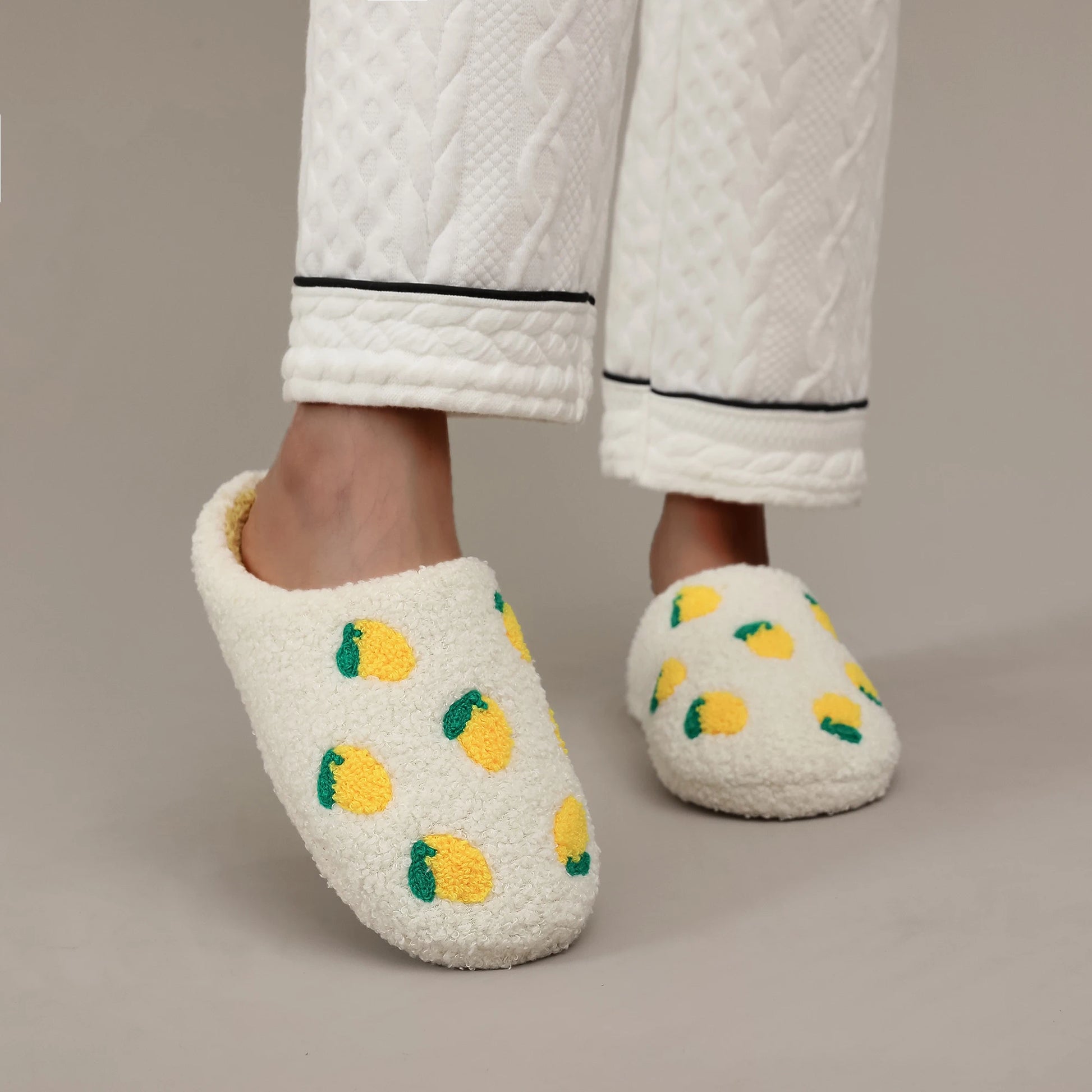 White slippers with yellow and green patterns worn with white pants on a beige background